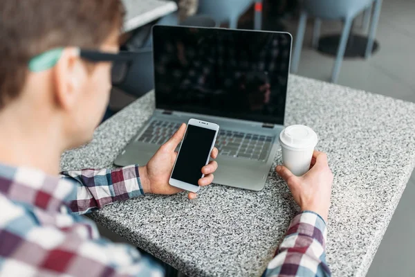 Un hombre se sienta en un café y trabaja en una computadora portátil, buscando trabajo, el estudiante escribe la tarea, un tipo con camisa y gafas — Foto de Stock