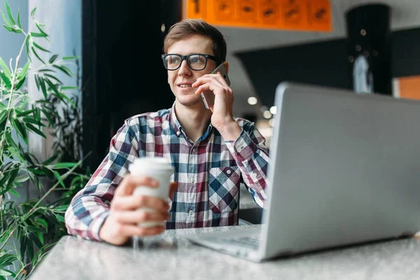 A man sits in a cafe and working on laptop, looking for work, the student writes the homework, a guy in a shirt and glasses