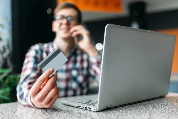 Um homem senta-se em um café com um laptop, fazer compras através da loja online, pagamento por cartão de crédito, um cartão de plástico — Fotografia de Stock