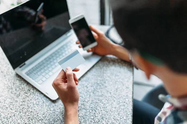 Ein Mann sitzt mit einem Laptop in einem Café, kauft über den Online-Shop ein, bezahlt mit Kreditkarte, Plastikkarte — Stockfoto