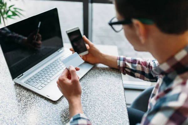 Un uomo si siede in un caffè con un computer portatile, fare acquisti tramite il negozio online, il pagamento con carta di credito, una carta di plastica — Foto Stock