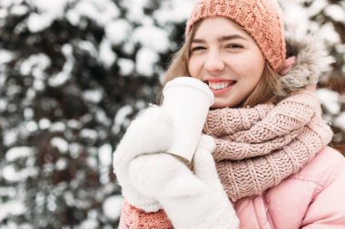 Güzel bir genç kız içme sıcak bir içecek, parlak kış day.woman gülümseyen ve mutlu, makro, ağaçlar, ilk kar beyaz örme eldivenler, açık havada, içinde portresi.