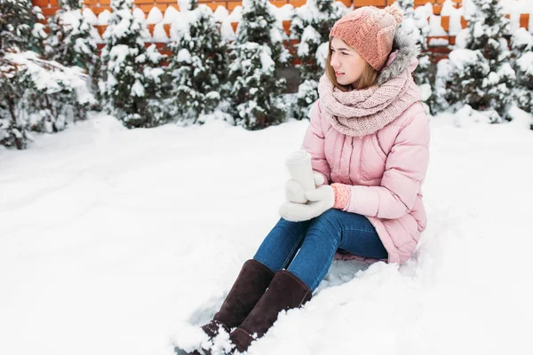 Porträtt av en vacker ung flicka i vit stickad vantar, Utomhus, hålla ett papper kopp med varm dryck, ljusa vinter day.the kvinna ler och är glad, närbild, träd i första snö i den. — Stockfoto