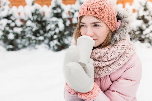 Porträtt av en vacker ung flicka i vit stickad vantar, Utomhus, dricka varm dryck, ljusa vinter day.woman leende och lycklig, makro, träd, första snön. — Stockfoto