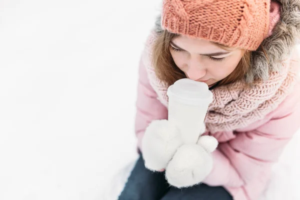 Retrato de uma menina bonita em mitenes de malha branca, ao ar livre, bebendo uma bebida quente, dia de inverno brilhante.mulher sorrindo e feliz, macro, árvores, primeira neve . — Fotografia de Stock