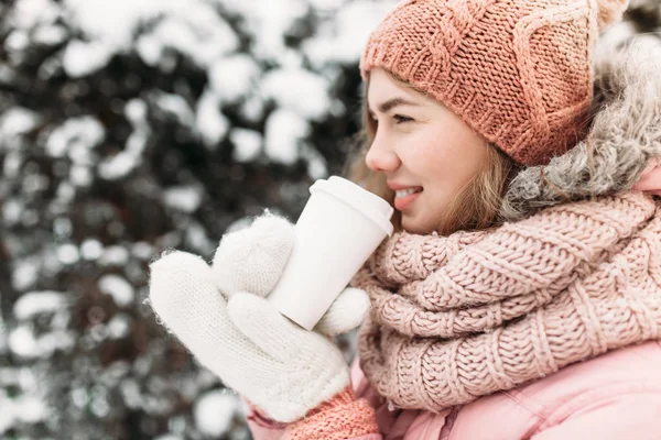 Porträtt av en vacker ung flicka i vit stickad vantar, Utomhus, dricka varm dryck, ljusa vinter day.woman leende och lycklig, makro, träd, första snön. — Stockfoto