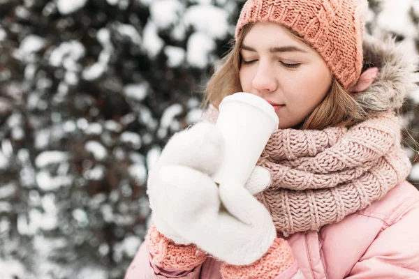Portrait d'une belle jeune fille en moufles tricotées blanches, en plein air, boire une boisson chaude, journée d'hiver lumineuse.femme souriante et heureuse, macro, arbres, première neige . — Photo