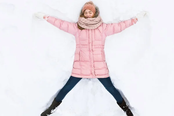 Mulher feliz deitado na neve e em movimento braços e pernas para cima e para baixo, criando a forma de um anjo da neve. Mulher sorridente deitada na neve nas férias de inverno, para publicidade  , — Fotografia de Stock