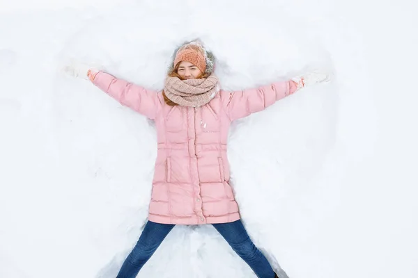 Mulher feliz deitado na neve e em movimento braços e pernas para cima e para baixo, criando a forma de um anjo da neve. Mulher sorridente deitada na neve nas férias de inverno, para publicidade  , — Fotografia de Stock
