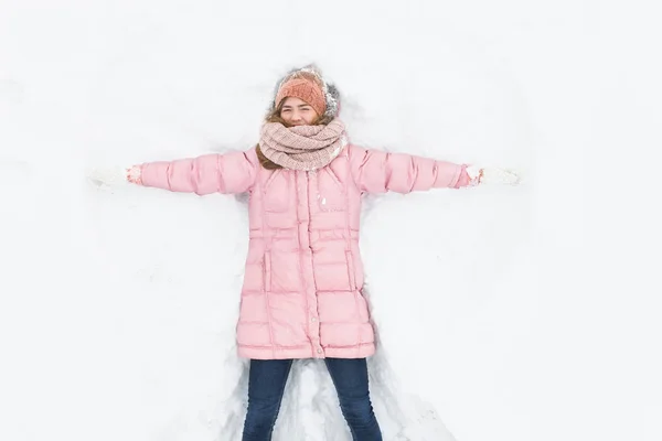 Mulher feliz deitado na neve e em movimento braços e pernas para cima e para baixo, criando a forma de um anjo da neve. Mulher sorridente deitada na neve nas férias de inverno, para publicidade  , — Fotografia de Stock