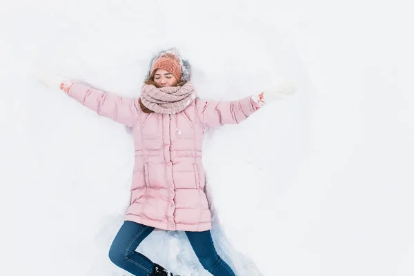 Mulher feliz deitado na neve e em movimento braços e pernas para cima e para baixo, criando a forma de um anjo da neve. Mulher sorridente deitada na neve nas férias de inverno, para publicidade  , — Fotografia de Stock