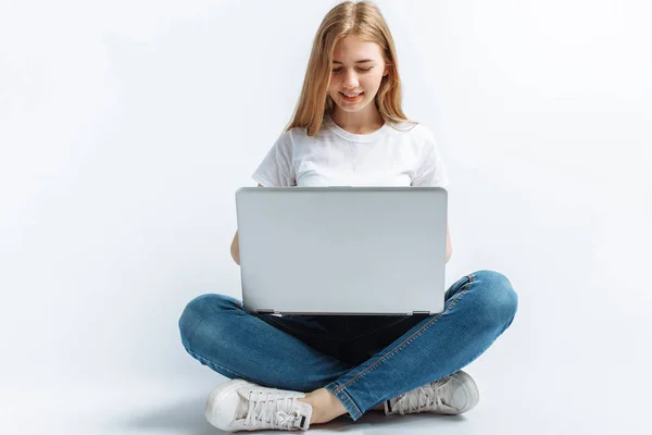 Hermosa chica sentada y escribiendo en el ordenador portátil, compras, en el estudio, fondo aislado —  Fotos de Stock