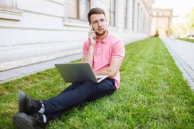 Evet, iş arama ve bir dizüstü bilgisayar ile şehirde çimenlerin üzerinde oturma yakışıklı adam
