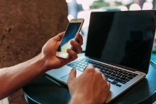 Zbliżenie dłoni, która posiada telefon, człowiek w kawiarni z laptopa, technologia — Zdjęcie stockowe