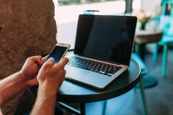 Zbliżenie dłoni, która posiada telefon, człowiek w kawiarni z laptopa, technologia — Zdjęcie stockowe