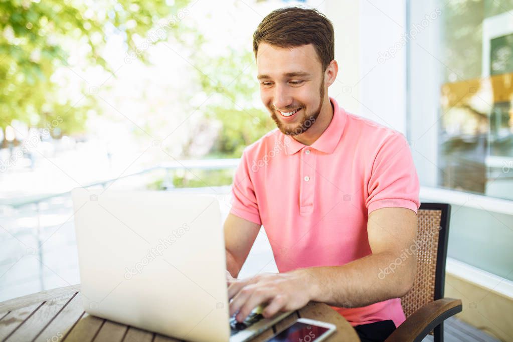 a young man sits in a cafe on the street, outdoors with a laptop