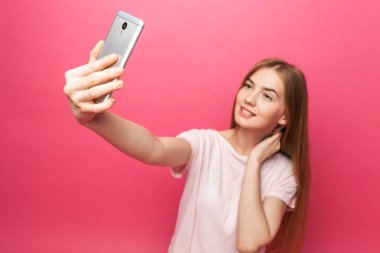 İzole üzerinde pembe bir arka plan, seyir telefon, yeterli, komik selfie, alarak fotoğraflandı, neşeli güzel kız, portre reklam