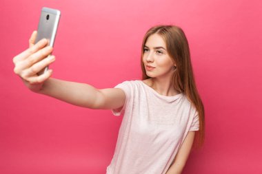İzole üzerinde pembe bir arka plan, seyir telefon, yeterli, komik selfie, alarak fotoğraflandı, neşeli güzel kız, portre reklam