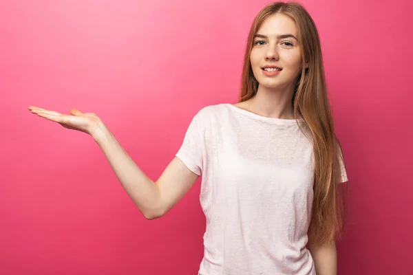 Крупним планом портрет щасливої блондинки, що показує передній палець на бік, стоїть на рожевому тлі, показує щось у порожньому копіювальному просторі для вставки тексту для реклами. — стокове фото