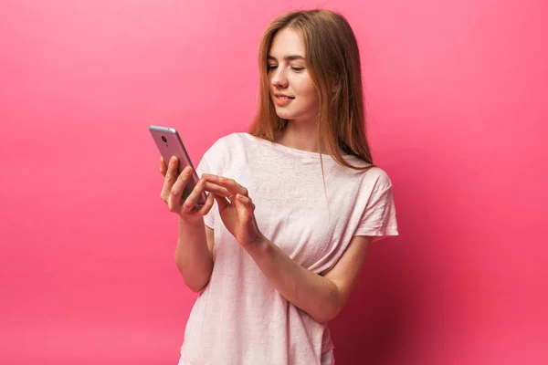 Retrato de alegre hermosa chica mirando el teléfono, mensajes de texto, aislado en el fondo rosa, publicidad — Foto de Stock