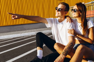 Genç bir adam ve bir kız şehirde asfaltta oturuyorlar. 