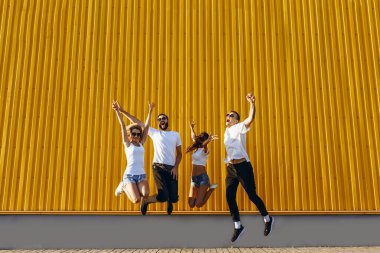 Mutlu genç arkadaşlar, erkekler ve kadınlar şehirde eğlenip zıplıyorlar.