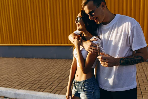Une fille et un gars en lunettes de soleil posent debout contre une wa jaune — Photo