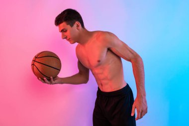 Basketbol oynayan genç atletik bir adam, arka planda n ile poz veriyor.