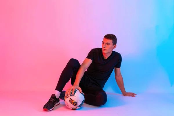 Jugador de fútbol en uniforme deportivo negro con pelota de fútbol sentado — Foto de Stock