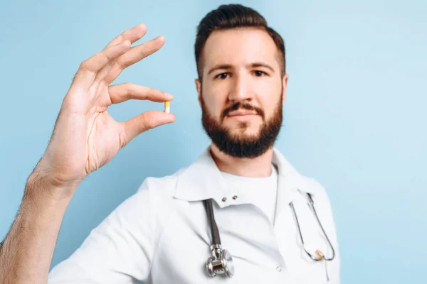 Gelukkig zelfverzekerde mannelijke arts het houden van een pil op een lichtblauwe rug — Stockfoto