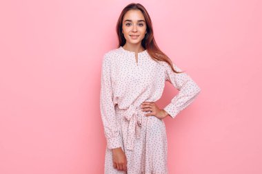 Şık giyinmiş genç bir kadın. Pembe arka planda poz veren kız