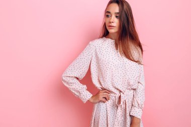 Şık giyinmiş genç bir kadın. Pembe arka planda poz veren kız