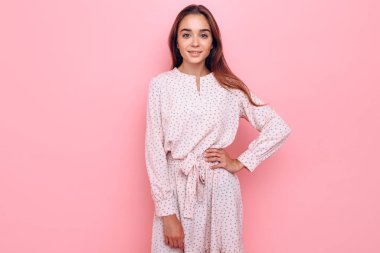 Şık giyinmiş genç bir kadın. Pembe arka planda poz veren kız