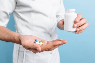 Mavi arka planda ilaç kavanozu olan bir doktor.