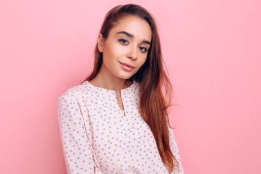 Şık giyinmiş genç bir kadın. Pembe arka planda poz veren kız