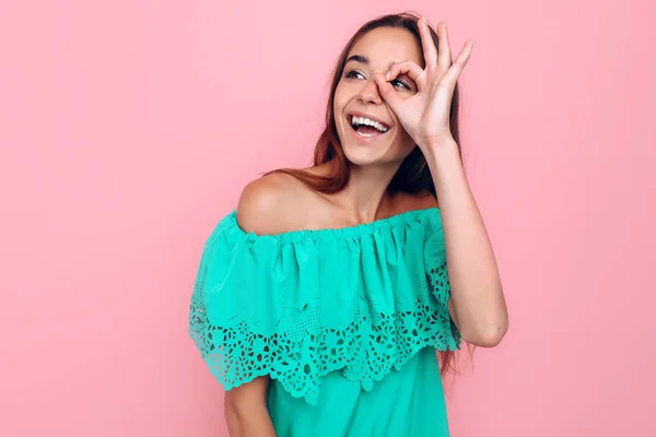 Mulher alegre atraente mostra OK, óculos de suas mãos em um fundo rosa — Fotografia de Stock