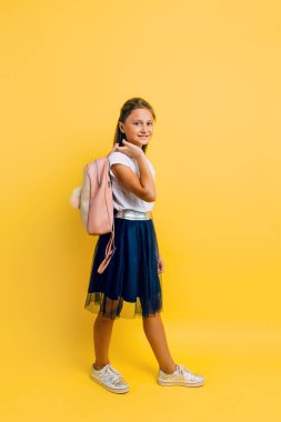 Portrait of a smiling little schoolgirl with a backpack on a yel