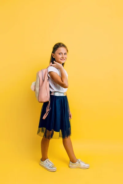 Portrait of a smiling little schoolgirl with a backpack on a yel — ストック写真