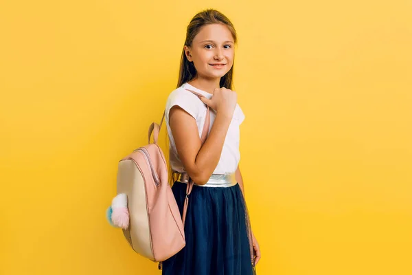 Portrait of a smiling little schoolgirl with a backpack on a yel — Stock Photo, Image