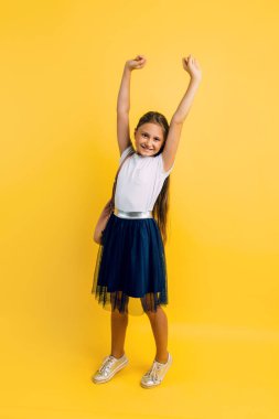 Charming little student on a yellow background. The pupil of a small child adores school. Emotional schoolgirl