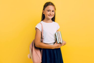 A teenager with a backpack and books. Stylish beautiful schoolgirl posing on a yellow background