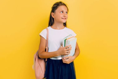 A teenager with a backpack and books. Stylish beautiful schoolgirl posing on a yellow background