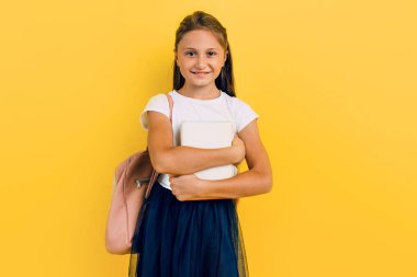 A teenager with a backpack and books. Stylish beautiful schoolgirl posing on a yellow background