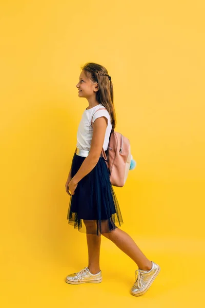 Portrait of a smiling little schoolgirl with a backpack on a yel — Stock Photo, Image