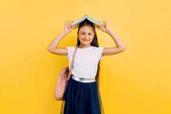 Adolescente positive tenant des livres sur sa tête, sur un fond jaune — Photo