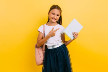 Purposeful teenage girl in school uniform, with a book on a yellow background.