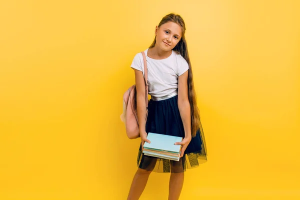 Lelah gadis remaja di seragam sekolah memegang banyak buku pada latar belakang kuning terisolasi Stok Foto Bebas Royalti
