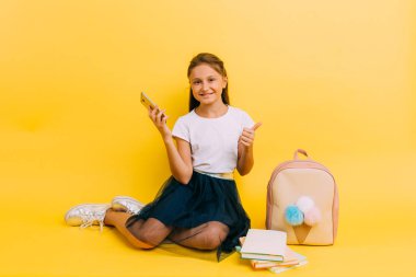 A little schoolgirl girl holds a smartphone in her hands and looks at the screen
