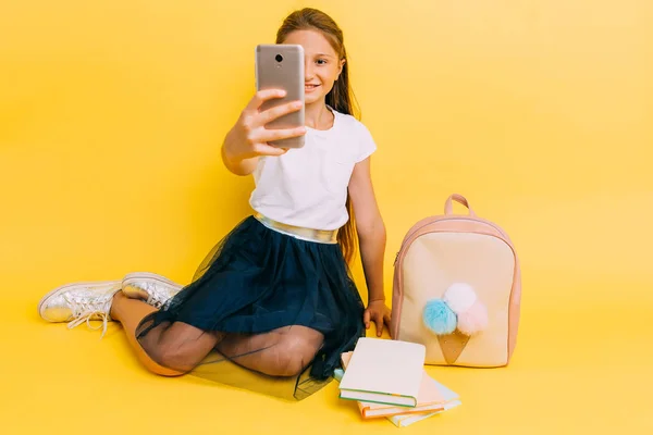 Kisiskolás lány csinál egy szelfit egy okostelefonon sárga alapon — Stock Fotó