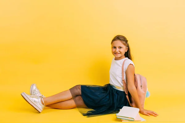 Happy teenage schoolgirl with books on a yellow background — Stock Photo, Image